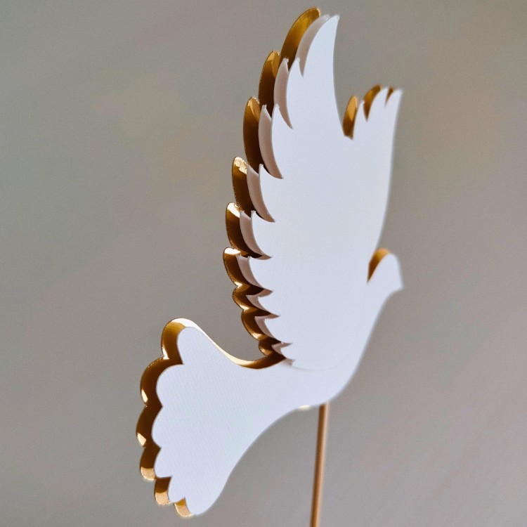 Elegancki, przestrzenny topper na tort w kształcie lecącego gołąbka (efekt 3D). Wzór wykonany z fakturowanego, białego papieru na podkładzie ze złotego lustra. Idealna, gotowa dekoracja na Chrzest Święty lub Komunię.