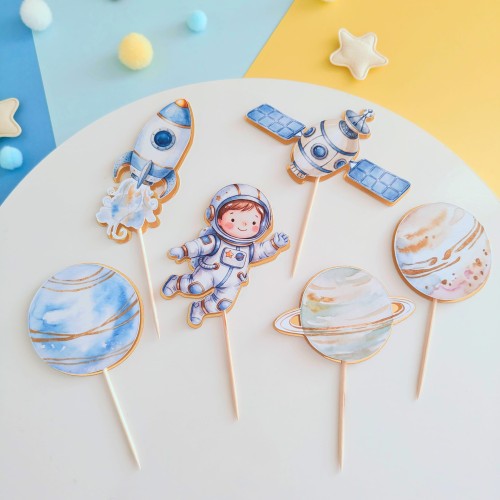 Zestaw 6 sztuk kosmicznych pikerów na babeczki i desery. Komplet zawiera różne ilustracje: astronautę, rakietę, satelitę i planety. Luksusowe wykończenie ze złotym, lustrzanym podkładem.